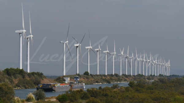 Container barge progressing in the heat waves along an alignment of wind turbines, Port Saint Louis du Rhône, southern France