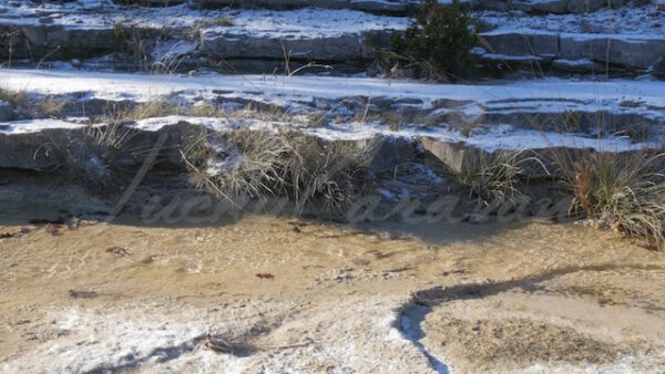 Small stream trickling through snow sprinkled rocky slabs in the scrubland