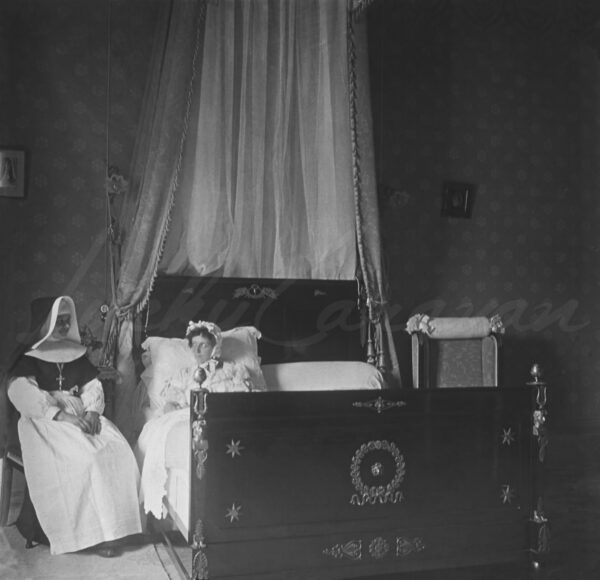 A nun visiting a bedridden woman in a room with bourgeois furnishings, circa 1910.