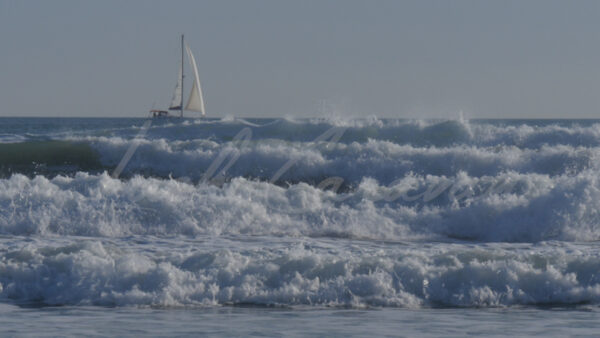 Sailboat progressing beyond big waves on the Mediterranean Sea, Occitania, southern France