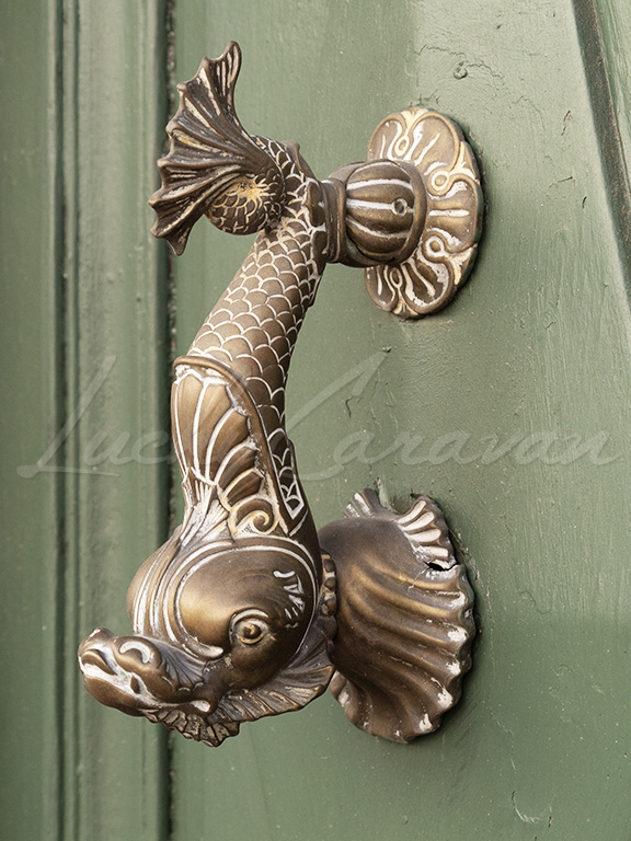 Antique knocker in the shape of a fish, on an entrance door.