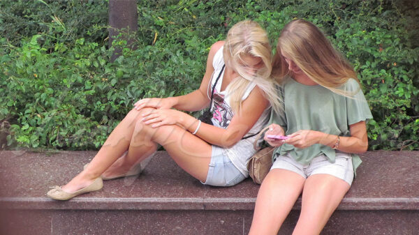 Two young blonde girls checking out a pink cell phone.