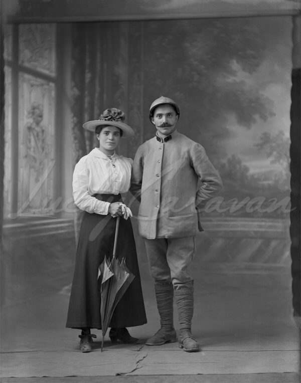 A French soldier and his wife during the Great War in a photographer's studio, circa 1916. The couple is standing on a painted soft-focus backdrop.