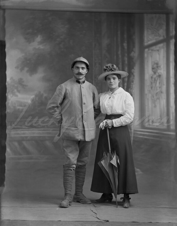 A French soldier and his wife during the Great War in a photographer's studio, circa 1916. The couple is standing on a painted soft-focus backdrop.