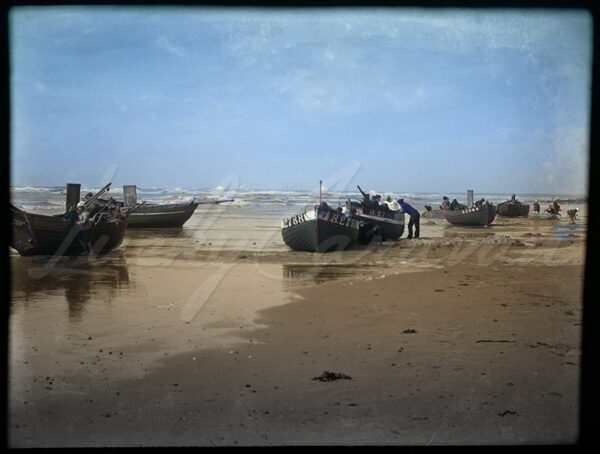 Strollers take advantage of low tide to approach fishing boats and collect shellfish in Pas-de-Calais, France, in the early 20th century.