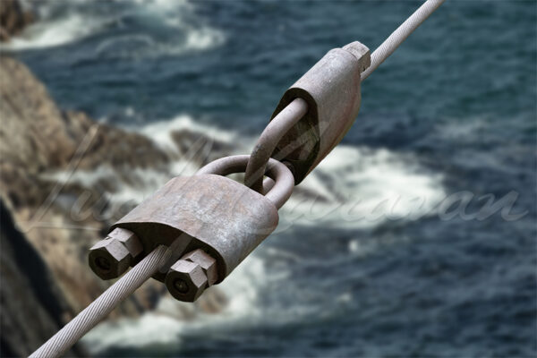 Fastening locks and cable on a suspension bridge over an ocean cliff.