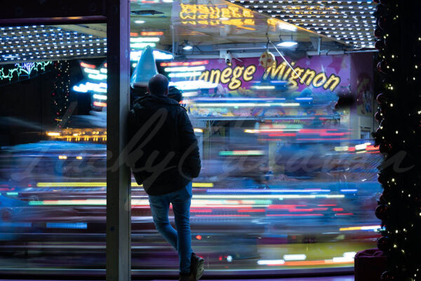 Young man standing in front of a merry go round at night.