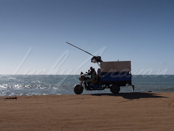Fisherman on his delivery tricycle observing the ocean.