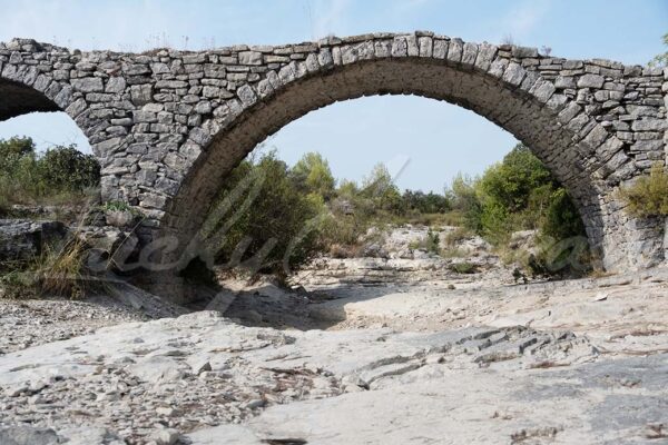 A dry riverbed beneath an old stone bridge.